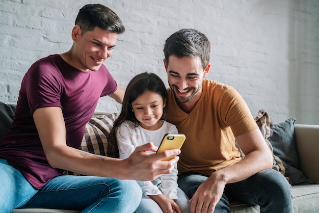 Coppia gay e la loro figlia che utilizzano un telefono cellulare a casa.