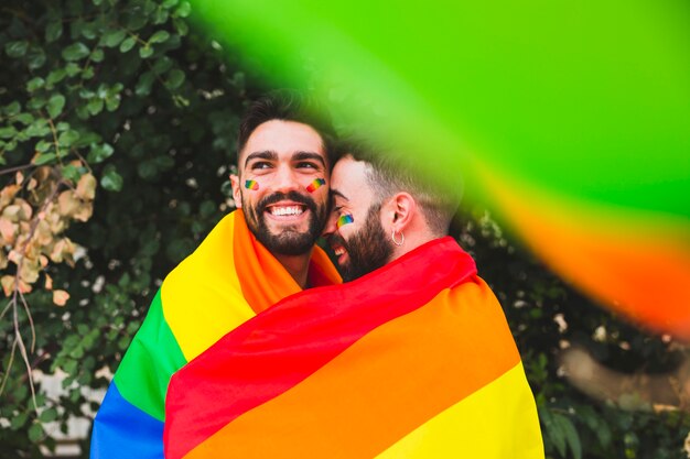 Gay couple with rainbow flag embracing on street