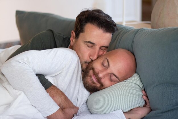 게이는 아침에 파트너와 함께 침대에 누워 키스를 합니다. 눈을 감고 누워서 깨어난 후 애인을 안고 있는 쾌활한 수염 난 남자의 중간 샷. LGBT, 사랑, 수면 주기 개념