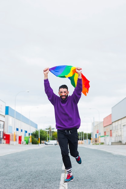 Foto gratuita uomo gay che funziona giù la strada che tiene la bandiera di lgbt sopraelevata