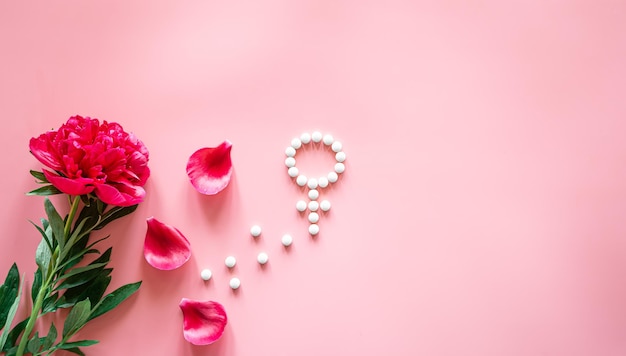 Free photo gender venus symbol made of pills and peony flower on a pink background