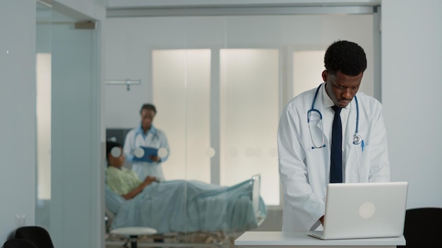 Врач общей практики смотрит на современный ноутбук для работы в системе лечения и здравоохранения. Врач использует устройство для поиска информации о проверке, чтобы вылечить пациента от болезни.