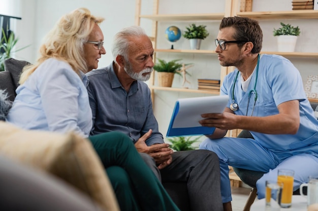 General practitioner showing to senior couple medical documents while being in home visit