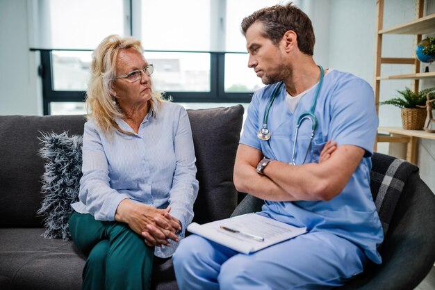 General practitioner with arms crossed communicating with mature patient about her medical test results while being in a home visit Focus is on woman