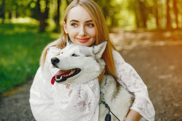 白い服を着た光の髪の優しい女の子が彼女の犬と一緒に遊んでいる