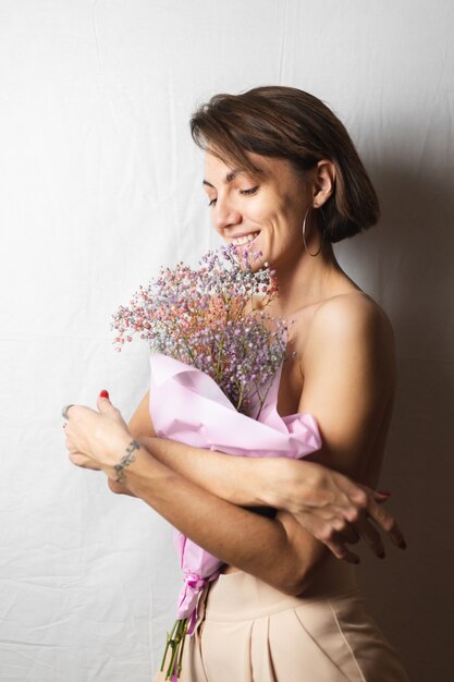 Gentle portrait of a young woman on a white rag topless holding a bouquet of dry multi-colored flowers and smiling cute, anticipation of spring