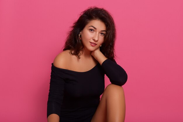 Gentle romantic female with confident look posing against pink wall