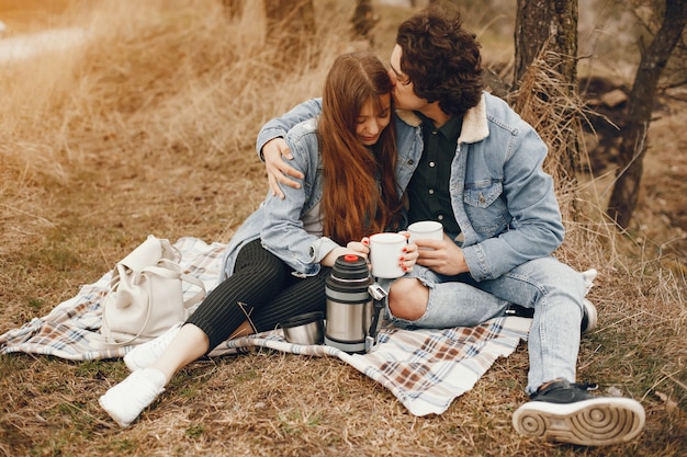 gentle and stylish couple sitting in the autumn park and drinking a tea