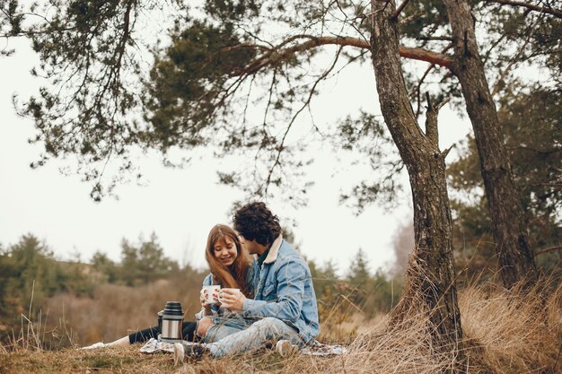 gentle and stylish couple sitting in the autumn park and drinking a tea