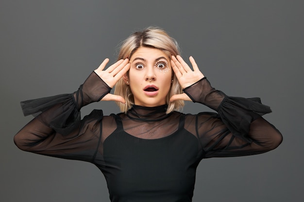 Genuine human emotions and feelings. Emotional beautiful blonde girl in trendy clothes and accessories expressing true astonished reaction on unexpected news, opening mouth in full disbelief