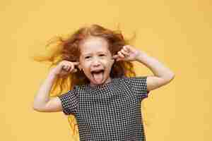 Free photo genuine human emotions, reaction and body language. angry spoiled little girl with red hair sticking out tongue, pretending not to hear you, plugging ears, screaming, being mad and naughty