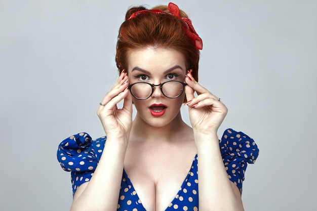 Free photo genuine human emotions and reactions. fashionable pin up girl wearing retro blue dress and red lipstick staring at you in astonishment