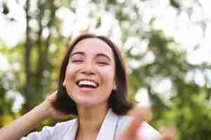 Foto gratuita gente genuina ritratto di donna asiatica che ride e sorride camminando nel parco sentendo gioia e positività