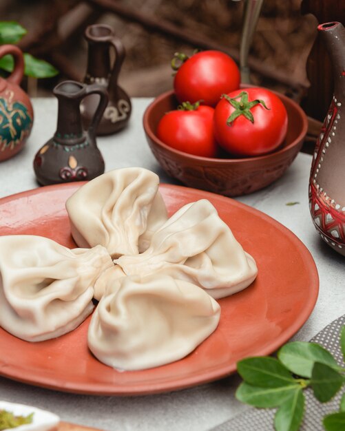 Georgian dough khinkali in red plate with tomatoes.