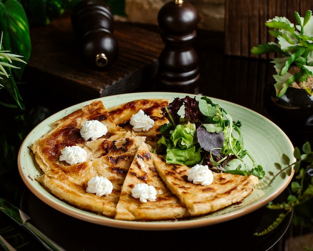 Fette di khachapuri georgiano condite con crema di formaggio, servito con insalata verde