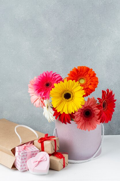 Цветы герберы ромашки в ведре с маленькими подарочными коробками рядом