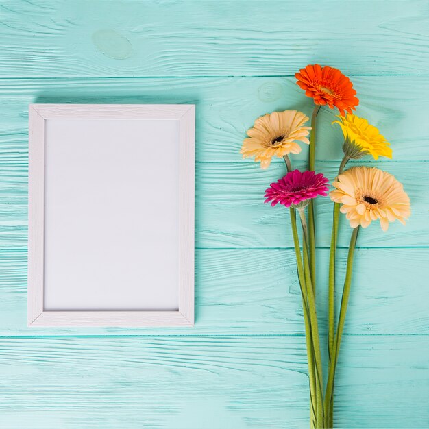 Gerbera flowers with blank frame on table