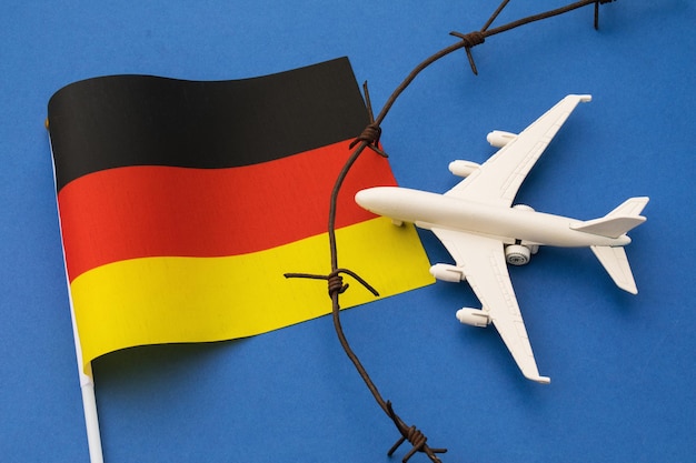 ドイツ​の​旗​、​青い​背景​の​有刺鉄線​と​おもちゃ​の​飛行機​、​州​の​航空​国境​違反​の​概念