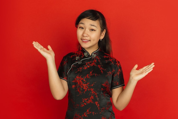 Free photo gesturing, inviting guests. happy chinese new year. asian young girl's portrait on red background. female model in traditional clothes looks happy. celebration, human emotions. copyspace.