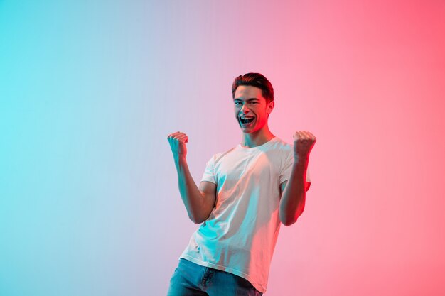 Gesturing. Young caucasian man's portrait on gradient blue-pink studio in neon light