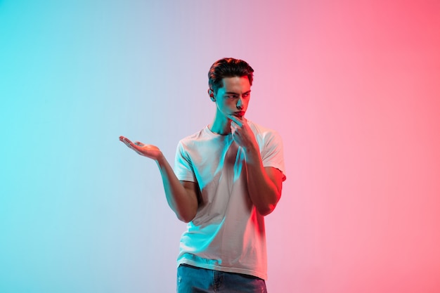 Gesturing. Young caucasian man's portrait on gradient blue-pink studio in neon light