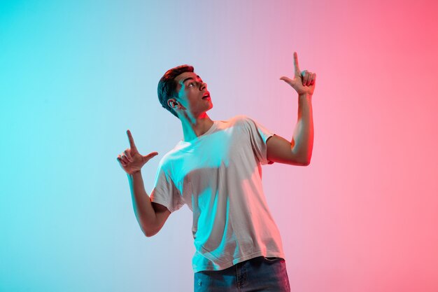 Gesturing. Young caucasian man's portrait on gradient blue-pink studio in neon light