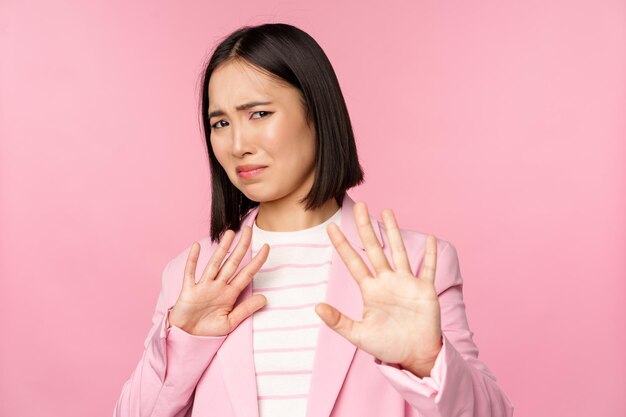 Get away Disgusted asian businesswoman rejecting shaking hands to refuse grimacing from dislike decline smth with aversion posing in suit against pink background