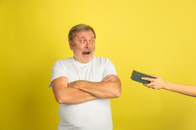 Getting a gift exciting. Caucasian man portrait isolated on yellow studio background. Beautiful male model in white shirt posing. Concept of human emotions, facial expression, sales, ad. Copyspace.