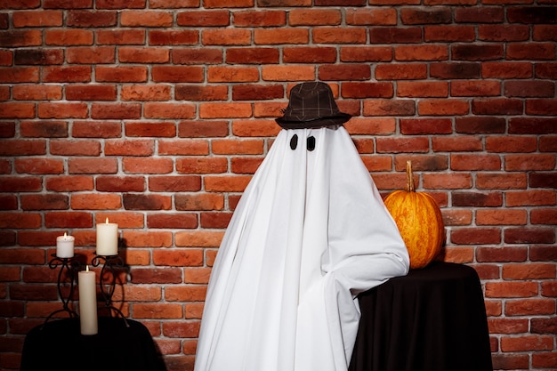 Free photo ghost in hat posing over brick wall halloween party.