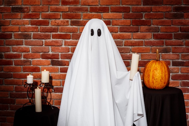 Ghost holding candle over brick wall. Halloween party.