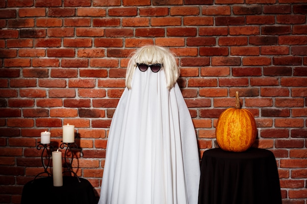 Free photo ghost in sunglasses and wig posing over brick wall