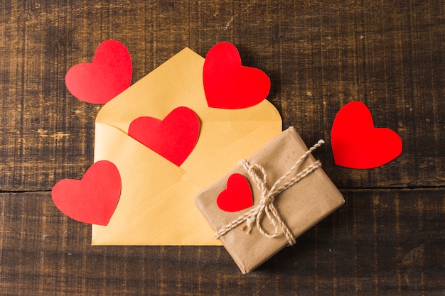 Gift box and envelope with red hearts on desk