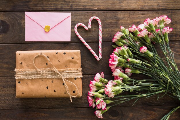 Подарочная коробка возле букета цветов, конверт и леденцы