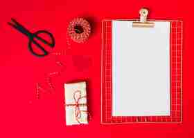 Free photo gift box near ornament heart, clipboard, scissors and threads