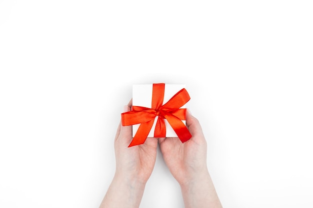 Gift box in a red ribbon in female hands on a white background top view