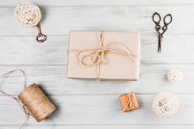 Free photo gift box; string spool scissor and decorative balls over white wooden desk