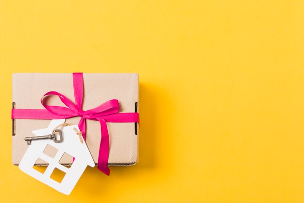 Gift box tied with key and house model over bright yellow background