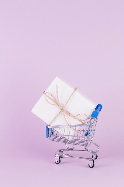 Gift box tied with string in shopping cart on pink background