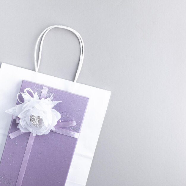 Gift box with a beautiful flower and a bow and a white package on a light background purple color top view
