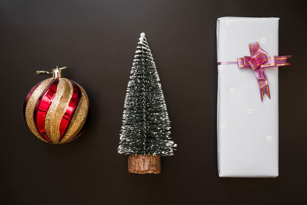 Подарочная коробка с бантом возле декоративного шара и елки