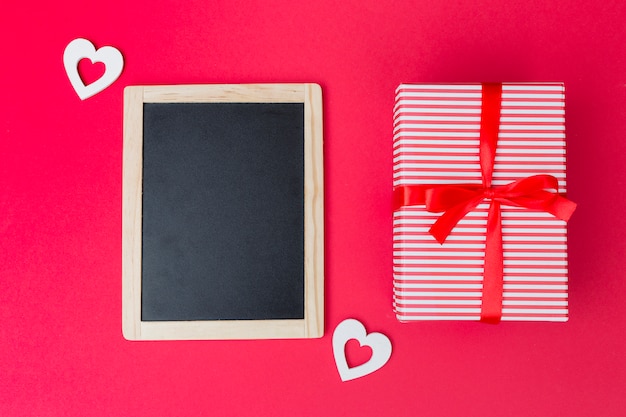 Gift box with chalkboard and white hearts on table