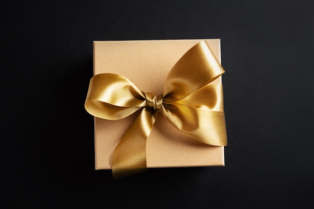 Gift box with golden ribbon on dark surface