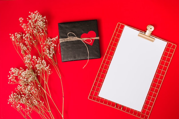 Gift box with ornament heart and clipboard near plants