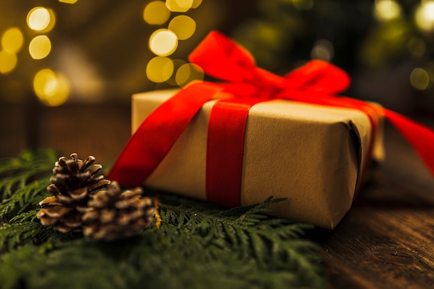 Gift box with red bow near branch on board