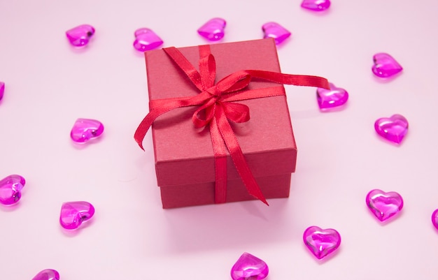 Gift box with red ribbon bow, on a pink background. hearts on a pink background