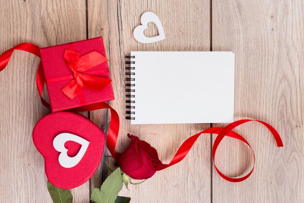Gift box with red rose and notepad on table 