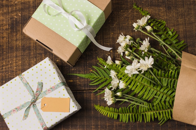 Gift boxed with flowers and leaves in paper bag over wooden table