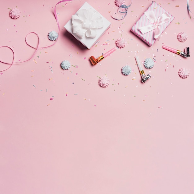 Gift boxes with candies and party blowers on pink background