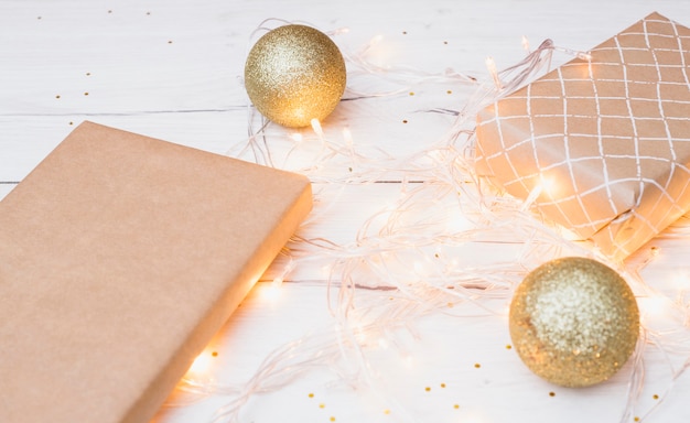 Gift boxes in wrap and Christmas balls near illuminated fairy lights