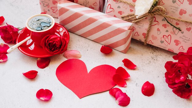 Gift boxes in wrap near flower petals, paper heart and cup with drink